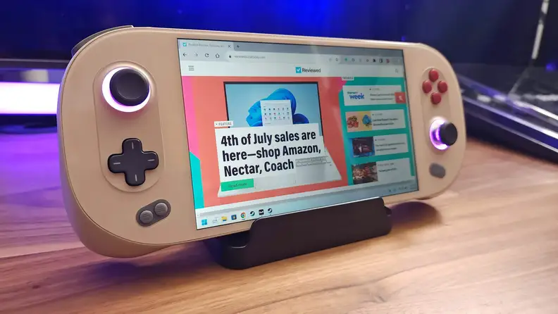 Ayaneo 2S Handheld gaming computer on top of stand on hardwood surface in front of colored LED light strip.