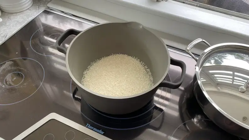 A Perfect Pot, filled with uncooked white rice, is sitting on top of an induction cooktop.
