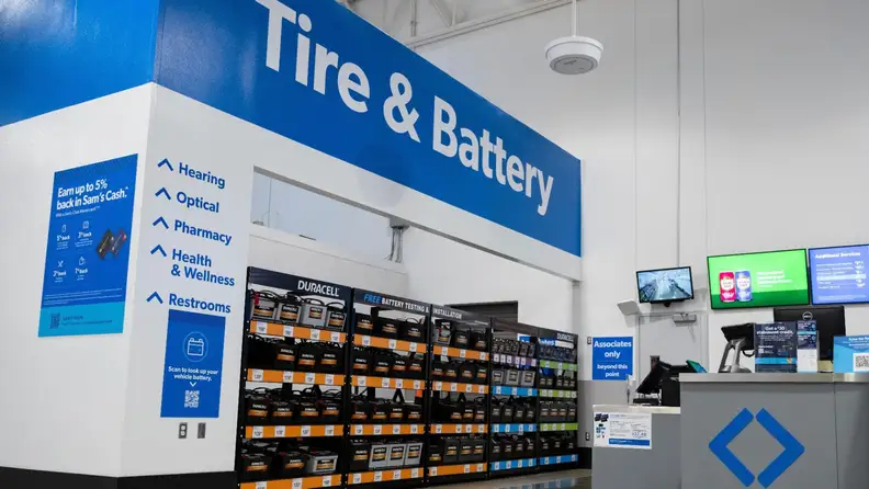 The Tire & Battery Center inside a Sam’s Club with shelves of Duracell batteries and signage for Optical, Pharmacy, and Health & Wellness.