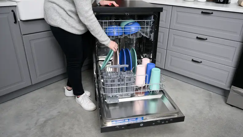The GE GPT225SSLSS portable dishwasher,open and being filled with colorful pastel dishes.