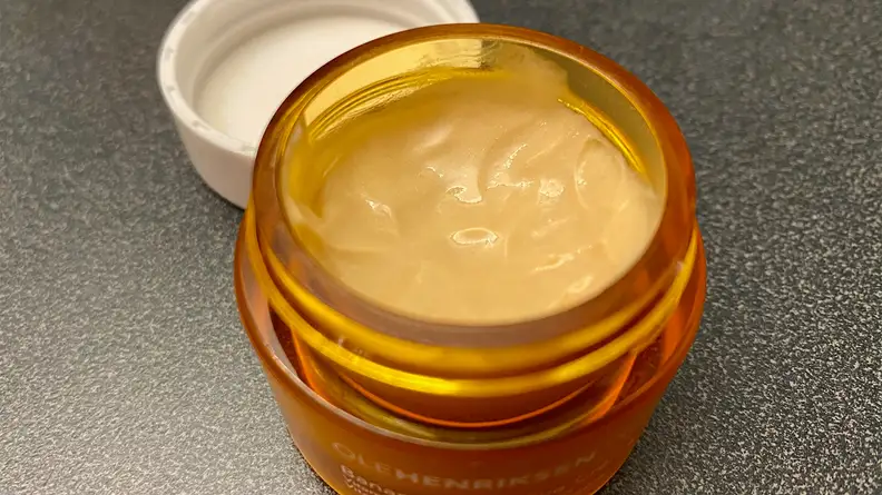 The OleHenriksen Banana Bright Eye Crème sitting on a bathroom vanity with its lid off to expose a orange-tinted cream.
