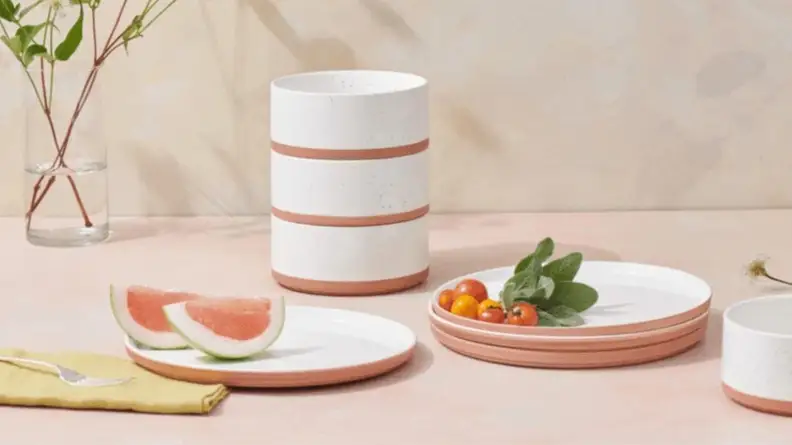 Spice colored Our Place bowls stacked next to plates with fruit and tomatoes.