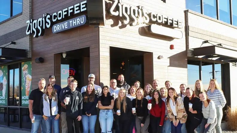 Group of people holding coffee cups outside a Ziggi's Coffee drive thru