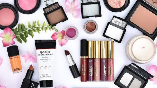 Assorted beauty products next to candle and flowers.
