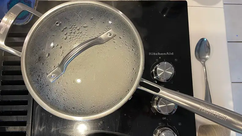 A Guy Fieri Flavortown Laser Titanium pot with lid attached boiling on top of cooktop.