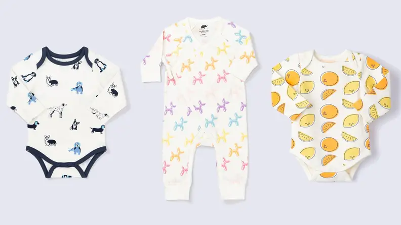 Three onesies lined up next to each other: long sleeved with no legs, white with blue puppies on them; a long sleeve and long pants onesie with multi-colored balloon animals on it; a long sleeved no pants onesie with orange and yellow fruits on it