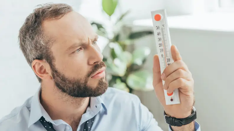 A man looks at a thermometer, utterly bewildered.
