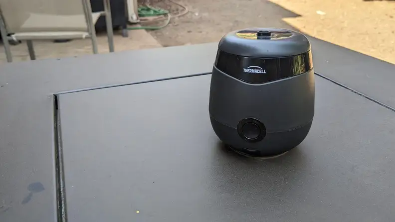 Black Thermacell E55 Mosquito Repellent device sitting on top of table outdoors on a sunny day.