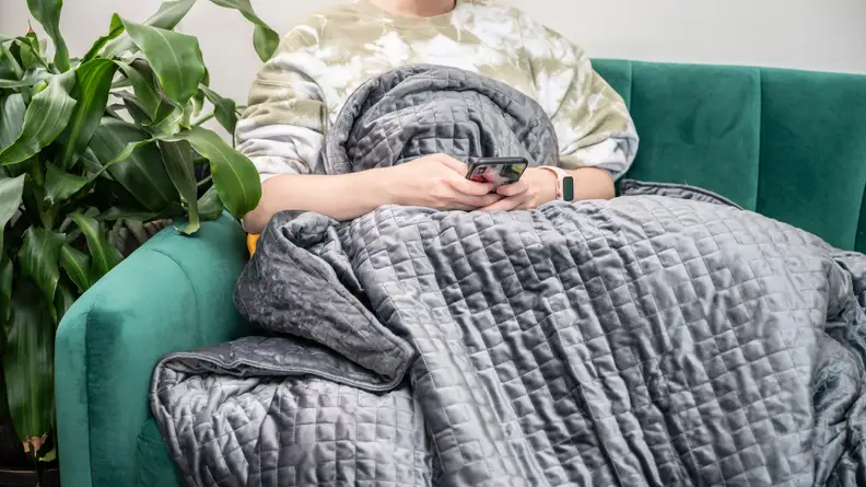 a woman sits under the gravity blanket on a green couch
