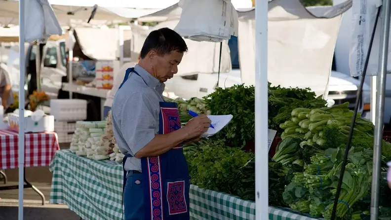 Farmer writing notes beside fresh produce stalls