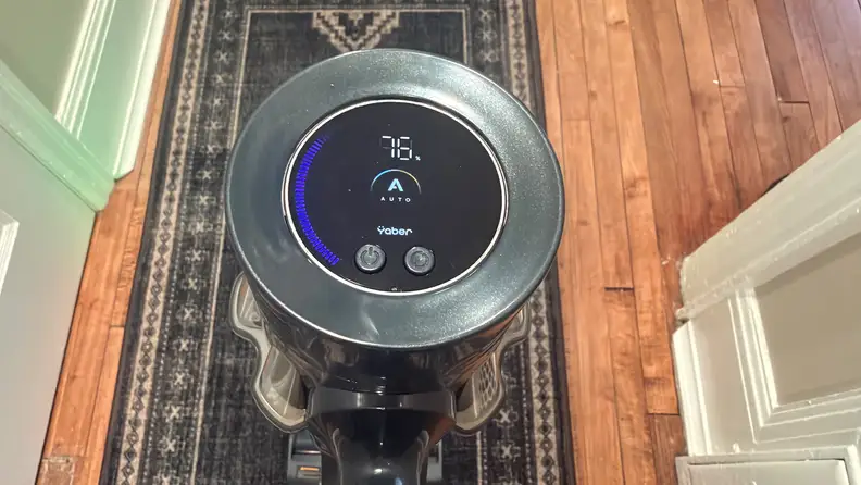Screen of Yaber HP20 cordless vacuum being used on a dark patterned rug on a wooden floor.
