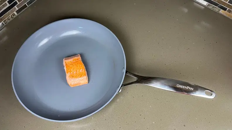 Small piece of uncooked salmon sitting in nonstick pan.