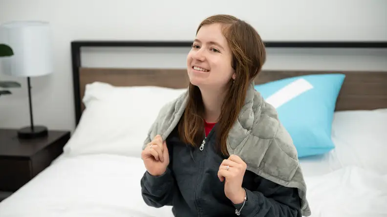 woman sitting up on bed holding grey blanket around her shoulders