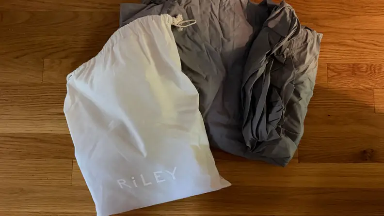 Grey Riley Home Percale Sheet Set shown with white carrying case on a wood floor.