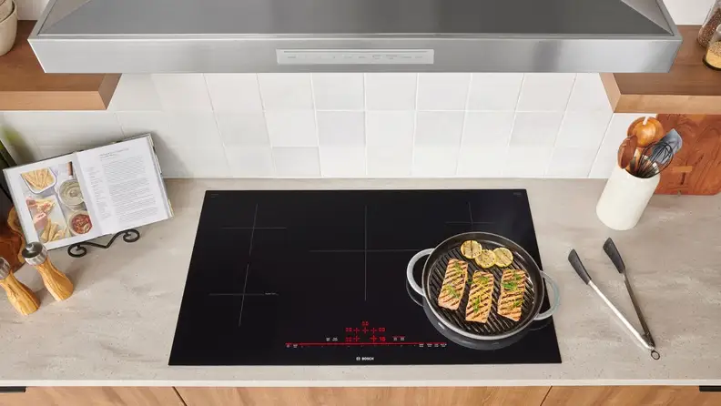 A top-down photo of an induction cooktop with a pan filled with fish cooking on top.