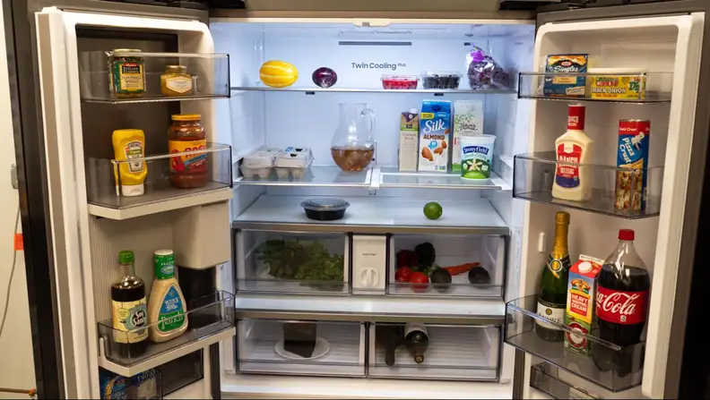 The french doors of a Samsung RF30 open showing inside fully stocked storage shelves and compartments.