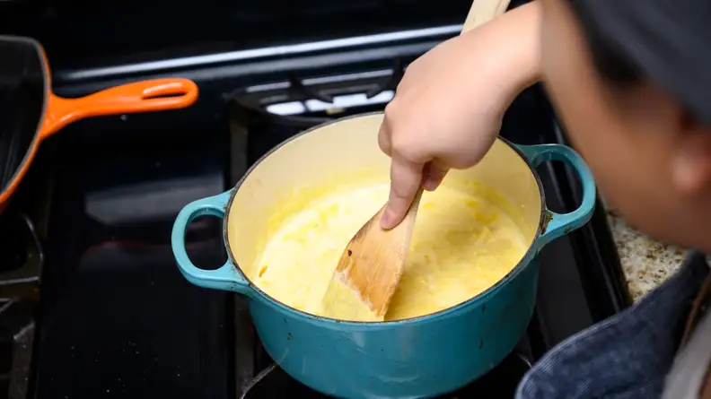 A person mixing pumpkin pie filling in a pot on a stove.