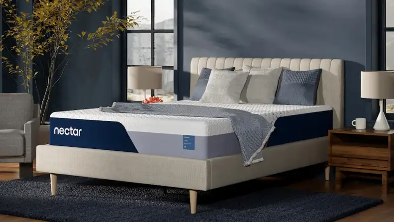 Nectar hybrid mattress with white top and navy blue base on a beige upholstered bed frame in a dark blue bedroom.