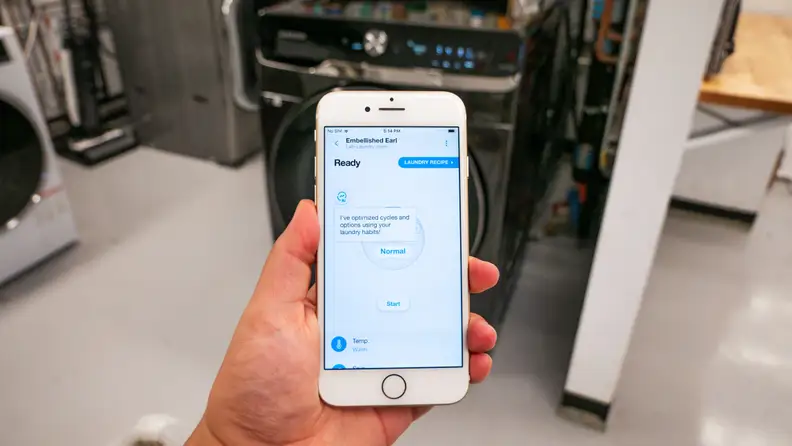 Person holding up smartphone with the Samsung smart app on screen with a wash cycle on screen.