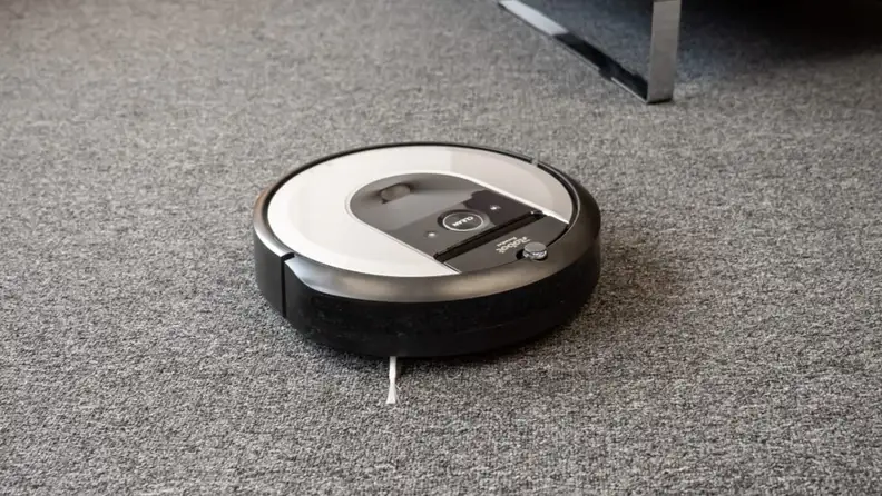 Silver and gray robot vacuum on carpeted floor.
