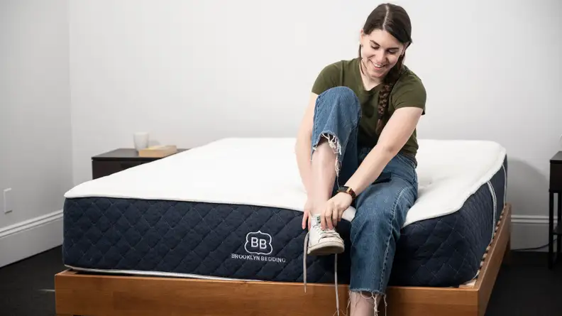 a woman sits on the foot of the Brooklyn Bedding Signature Hybrid tying her shoes