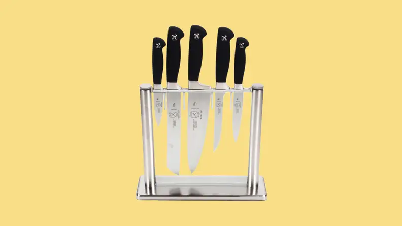 Five knives of various sizes stored in a glass block against yellow bacgkround