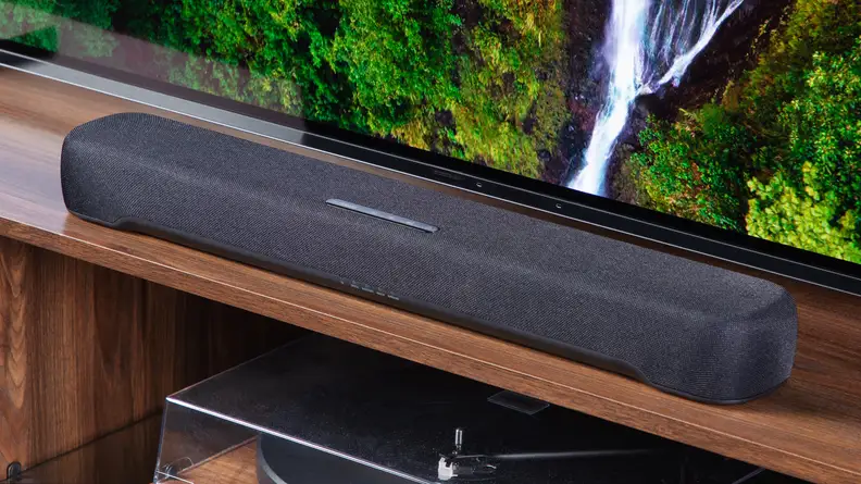 The Yamaha SR-C30A on a wooden table in front of a TV shot from an angle to the right.