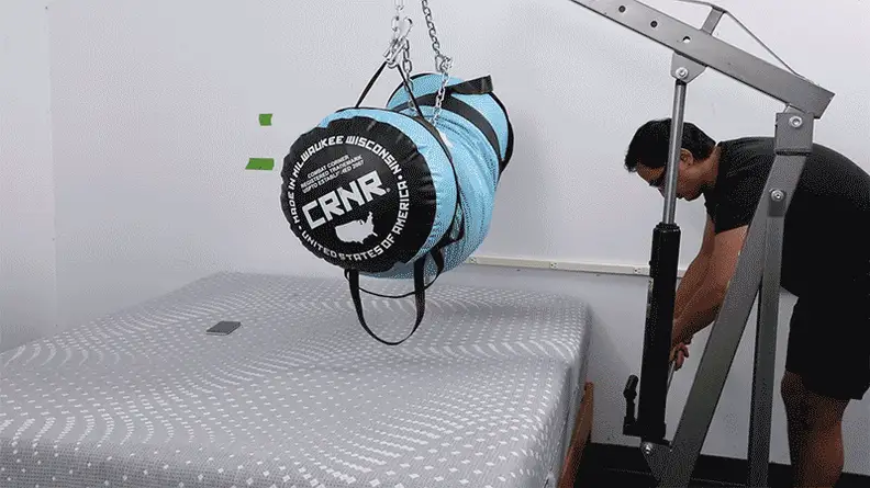 A person lowering a weighted punching bag onto the Sealy Posturepedic mattress to test its absorbency.