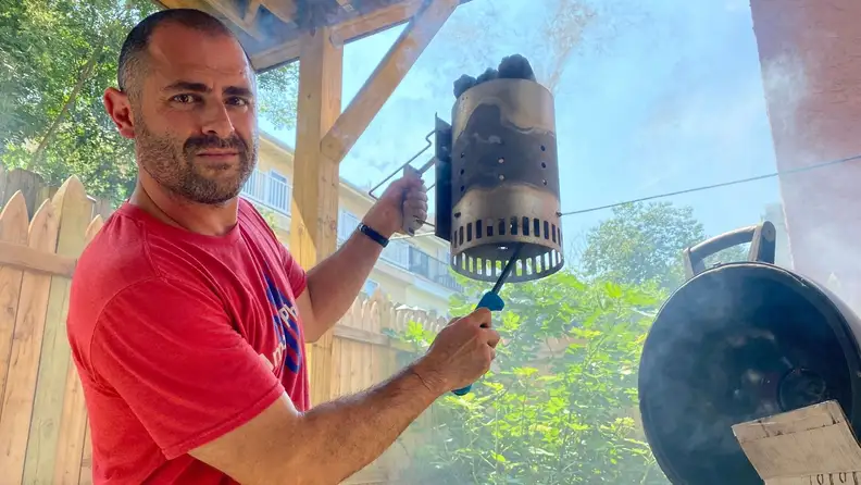 A person holds a container of charcoal in one hand as they hold a lighter in the other hand.