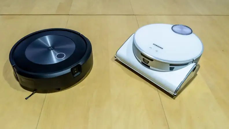 iRobot and a Samsung robot vacuum sit on a yellow table surface