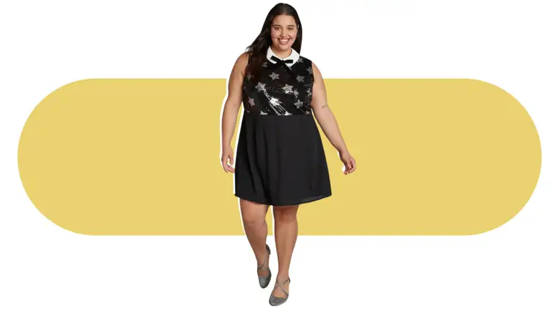A model wearing a black dress that features silver stars along the bodice, with a white Peter Pan collar and black bow tie.
