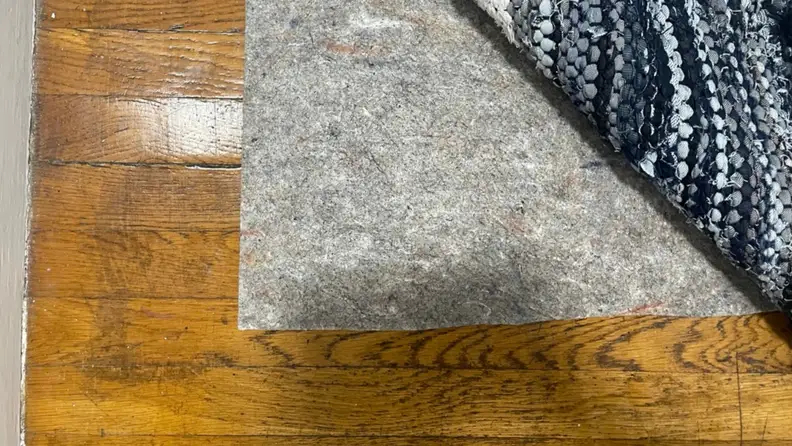 The corner of a woven rug flipped up to reveal a rug pad.