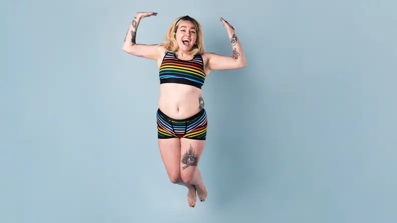 A person jumping up in the air against a blue background in TomboyX underwear.
