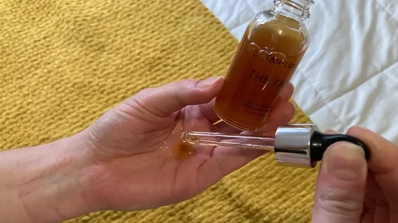 Person squeezing serum into palm of hand while holding bottle.