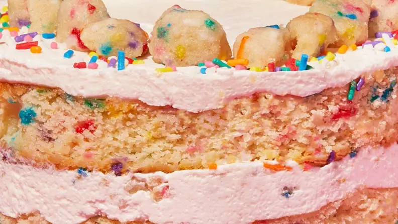 A closeup image of funfetti birthday cake with layers of creamy vanilla frosting.