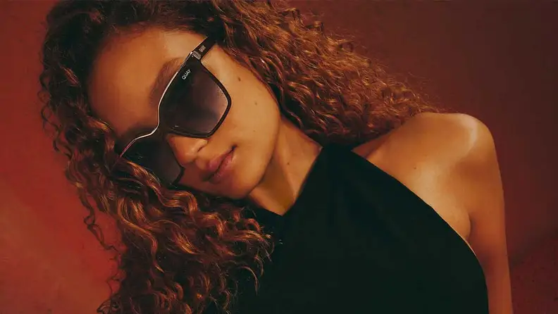 Woman wearing Quay Level Up sunglasses in a dark red background.