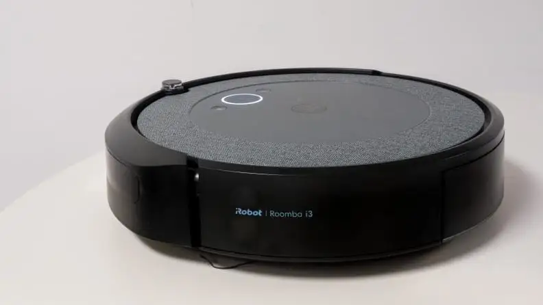 The iRobot Roomba i3 vacuum is circular, with a gray shell and a black bumper around it.