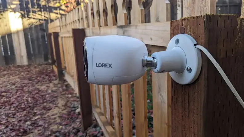 A side angle view of the Lorex 4K Dual-Lens Wi-Fi Security Camera hanging on a fence outdoors.