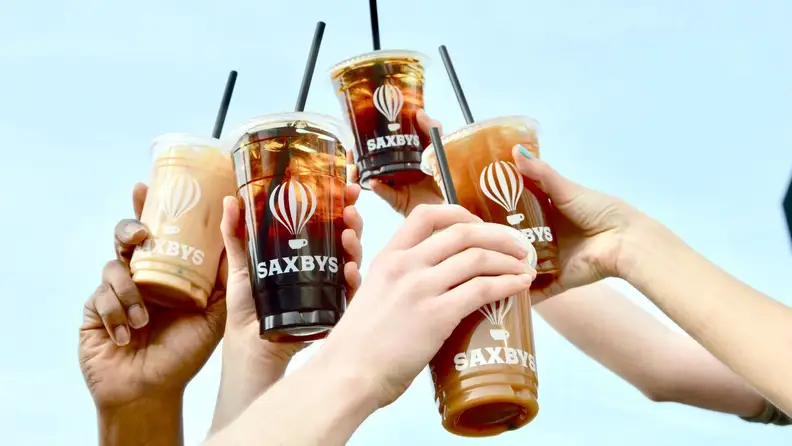 Hands holding up iced coffee drinks with branded cups