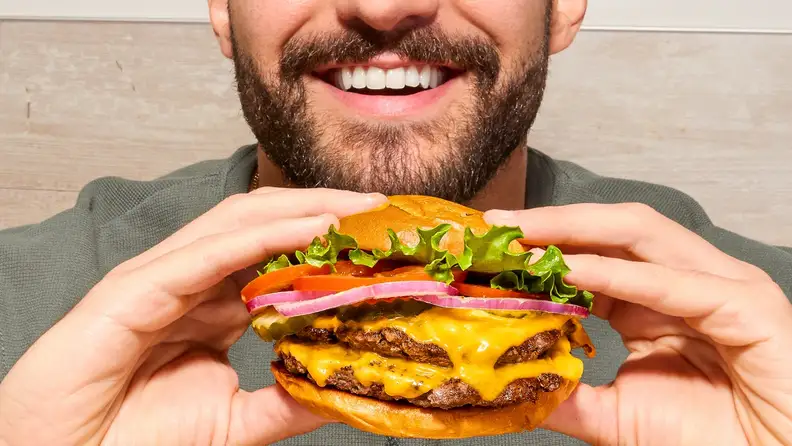 A man holding a double cheeseburger up to take a bite