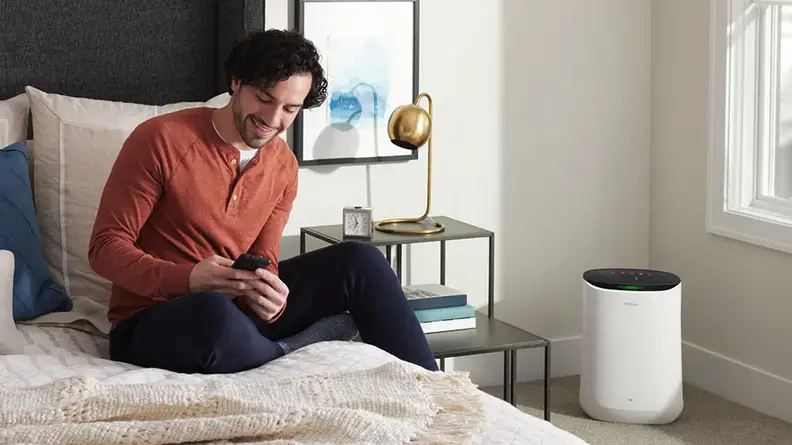 Person sitting on top of bed in bedroom while smiling at smartphone.