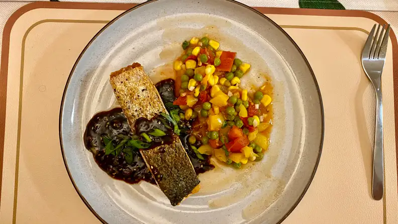 A plate of grilled salmon, succotash, and parsley sauce sits on a placemat.