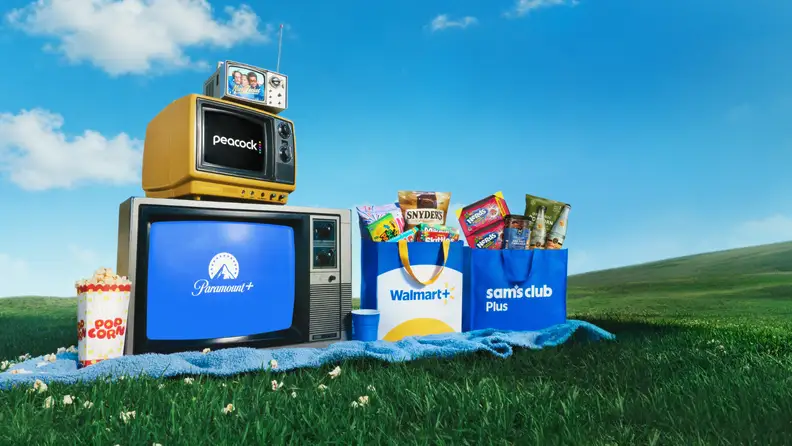 Retro TVs displaying Peacock and Paramount+ logos next to Walmart+ and Sam’s Club Plus tote bags filled with snacks on a grassy hillside