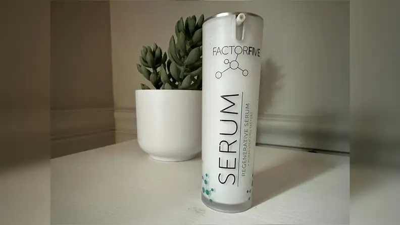 Bottle of FactorFive Regenerative Serum on a white surface with a small green plant in the background.