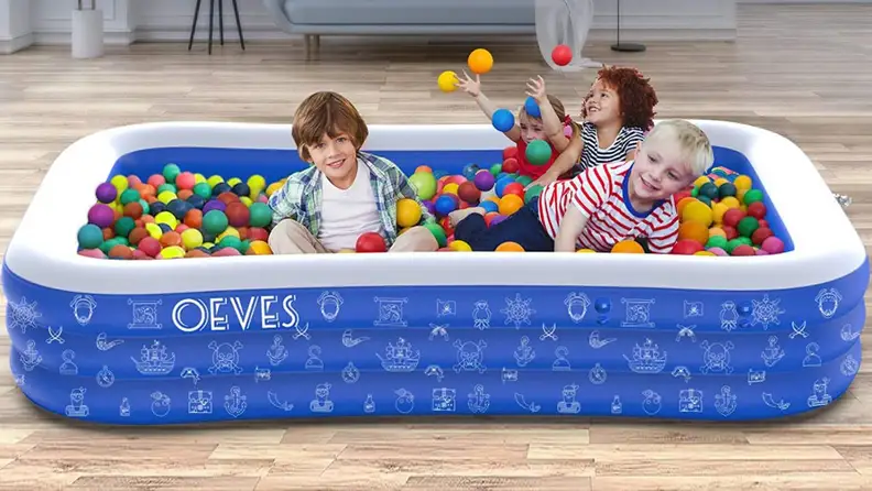Four children play in an inflatable pool filled with plastic balls.