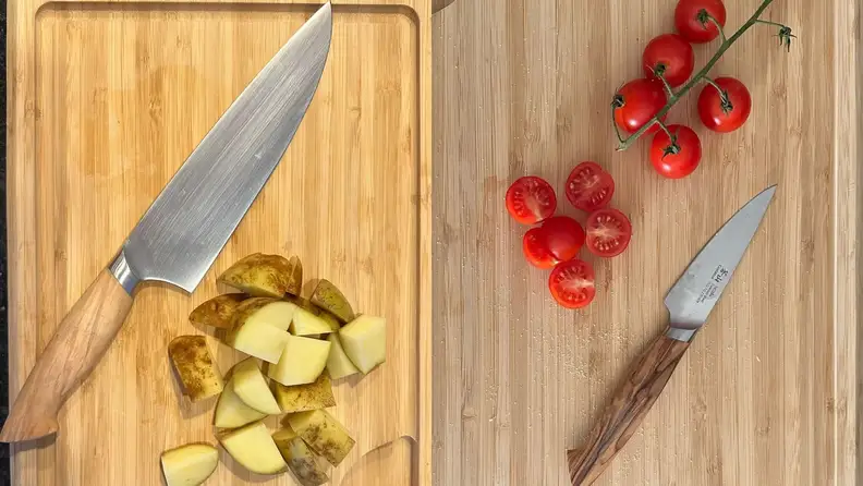 Two Cangshan knives on cutting boards next to chopped vegetables.