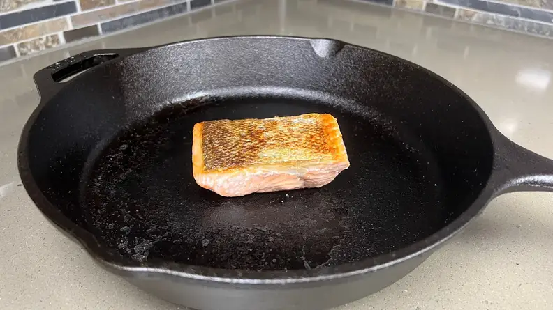 Small piece of salmon cooking in cast iron pan.