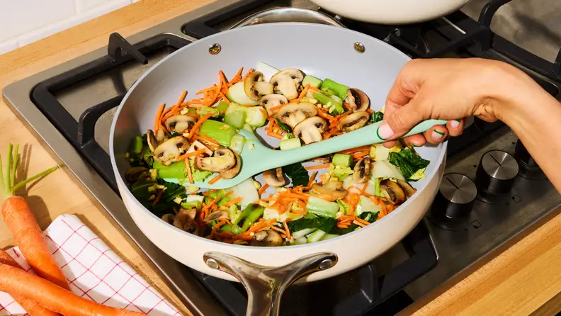 Person cooking colorful veggies in a nonstick pan while preparing one of the HelloFresh recipes at home.