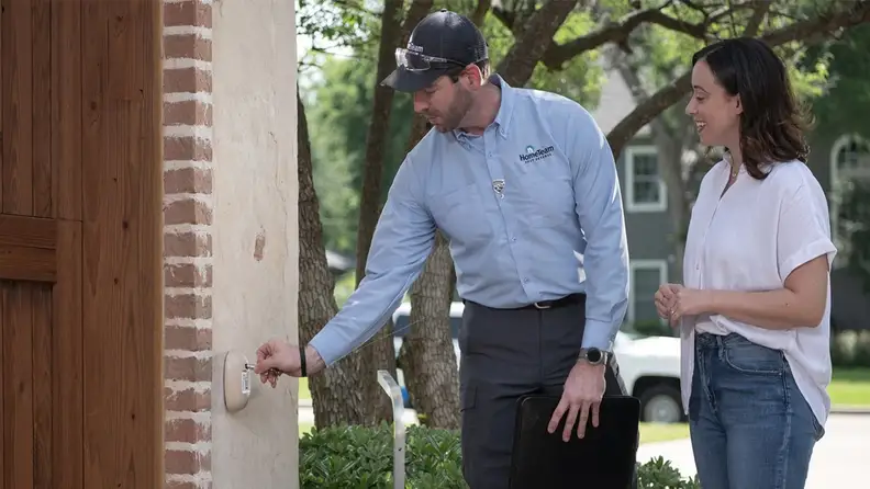 Technician installing a pest monitoring device on exterior wall