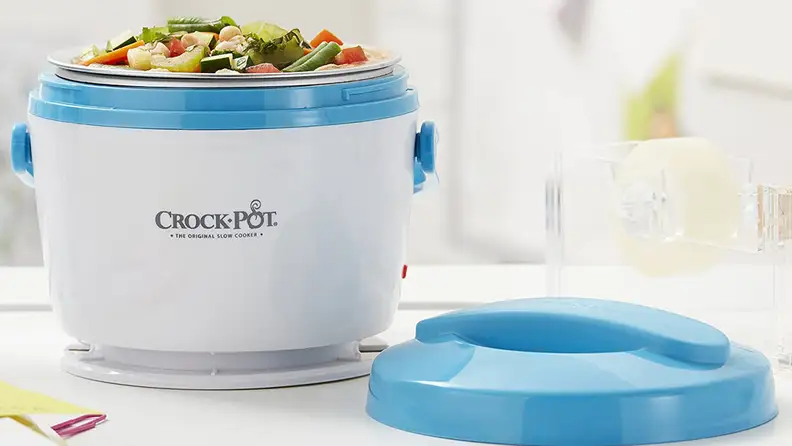 An personal-size Crock-Pot sits open on a table, with its lid beside it. It is full of a vegetable soup.